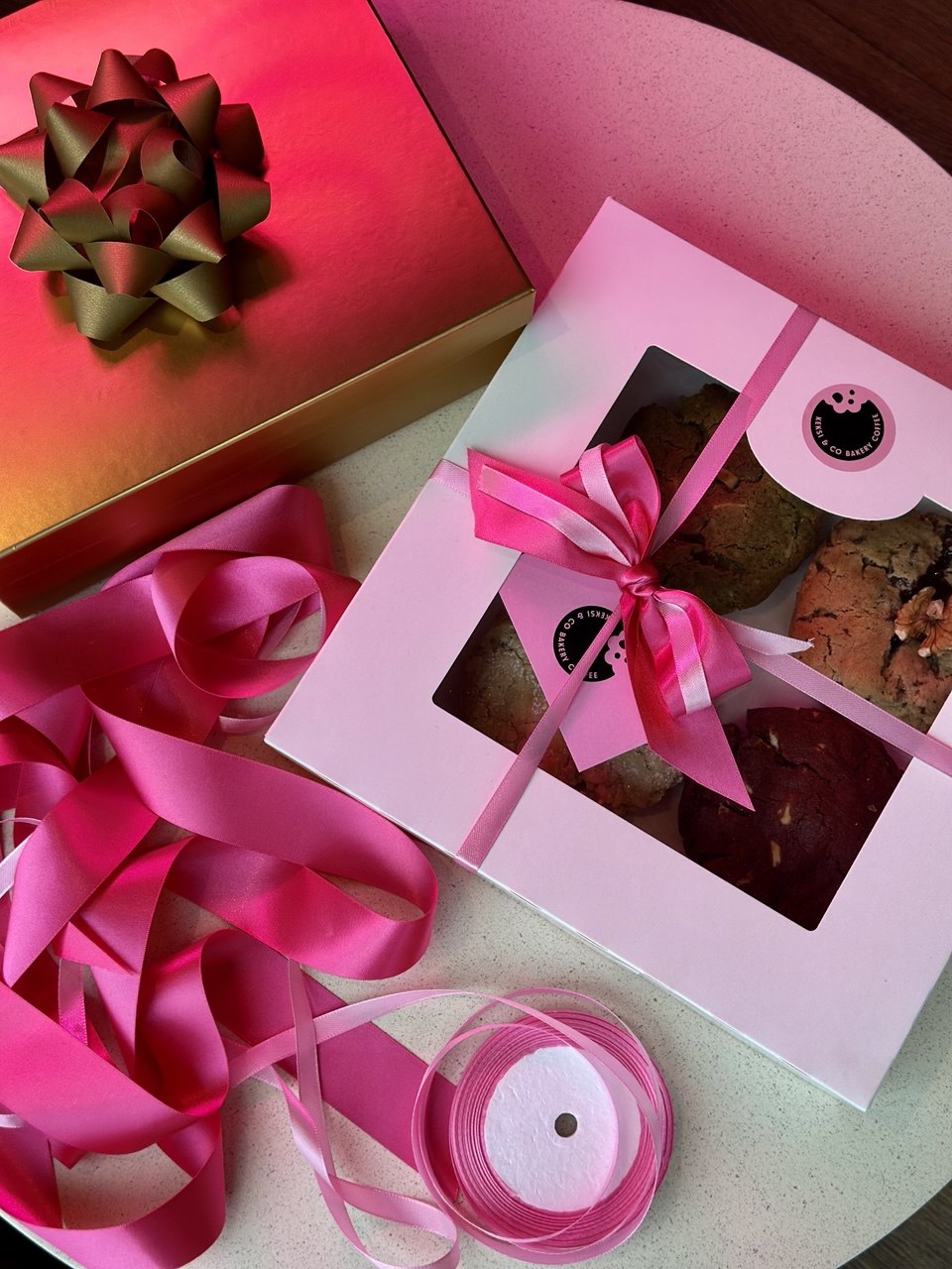 Keksi & Co gift cookie box wrapped with a pink ribbon, next to a gift bow